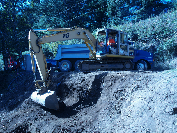 An excavator at the top works in tandem with spiderhoe to move debris up the hill